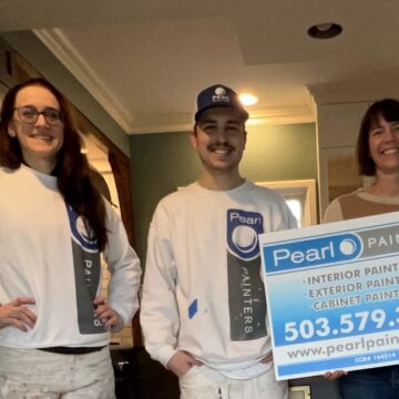 Three people stand indoors, two in painters' uniforms and one holding a sign for "Pearl Painters" with contact information and services listed.