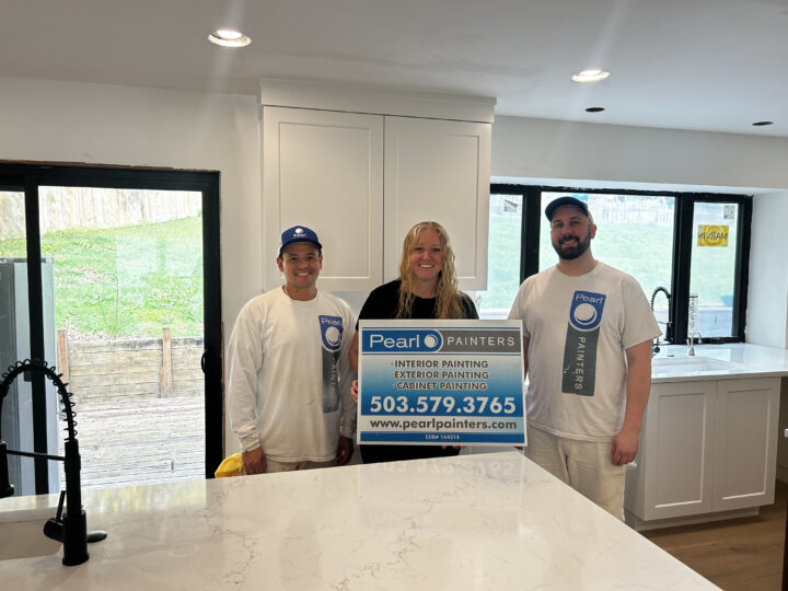 Three people in a modern kitchen hold a Pearl Painters sign for painting services in Portland, showing phone and website.