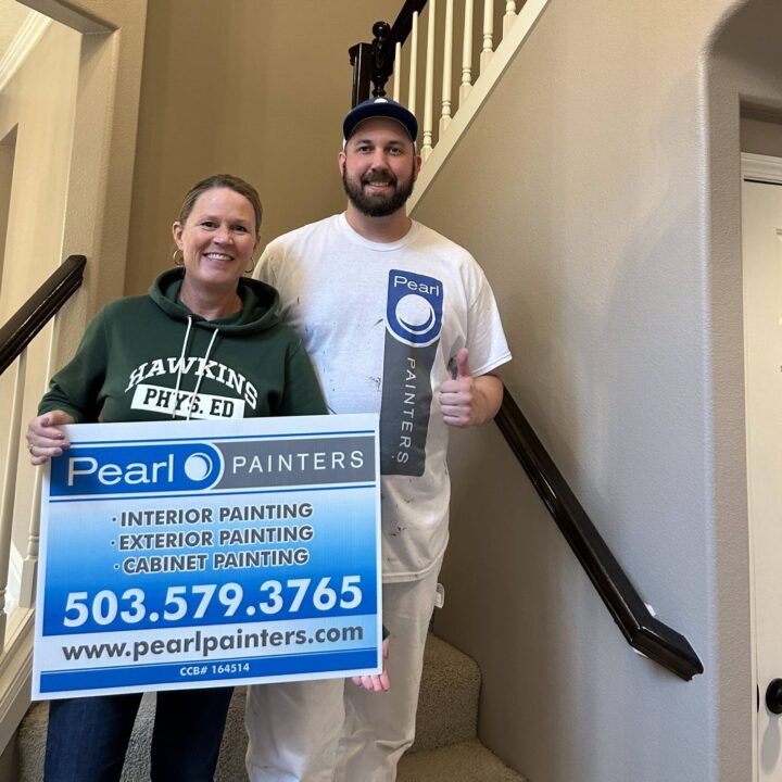 Two people on a staircase, one holding a Pearl Painters painting service sign with contact info; location appears to be indoors.