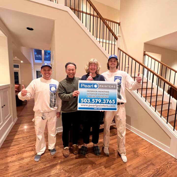 Four people stand on a wooden floor in Portland; two painters in uniform hold a Pearl Painters sign, all giving thumbs up.