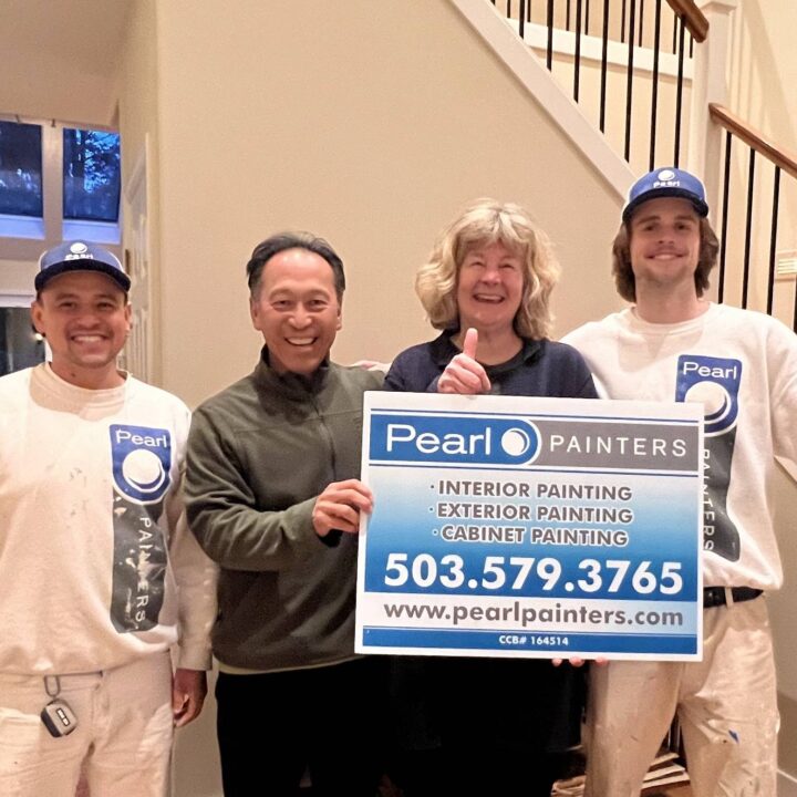 Four people indoors, two in Pearl Painters uniforms, two holding a Pearl Painters painting services sign in Portland.