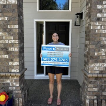 Person in front of Featherstone house holds Pearl Painters sign for Portland painting services, available through Aug 2025.
