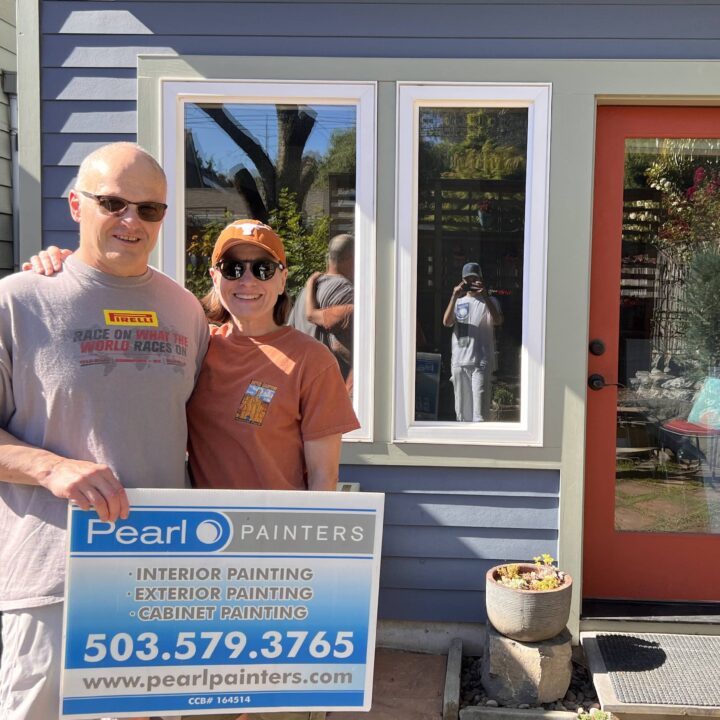 Two people hold a Pearl Painters sign outside a house; a third takes the photo, visible in the door reflection. Likely Portland.