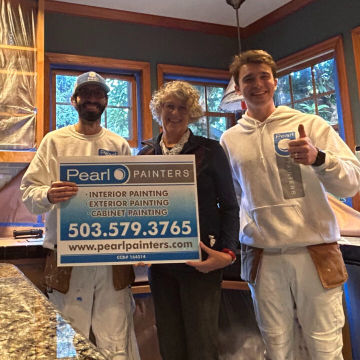 Two painters in Pearl Painters uniforms hold a painting service sign with phone number; three people in a Portland kitchen.