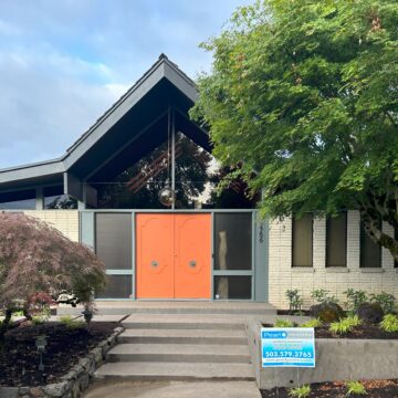 A modern house with a steeply pitched roof, orange double doors, and a lush green tree in the front yard invites you in. A sign near the entrance displays a painting company’s contact information, reminding passersby to book early for their next exterior project before the heat sets in.