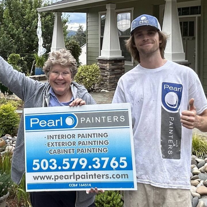 Two people outside a house in Portland hold a Pearl Painters sign for painting services, showing phone number and website.