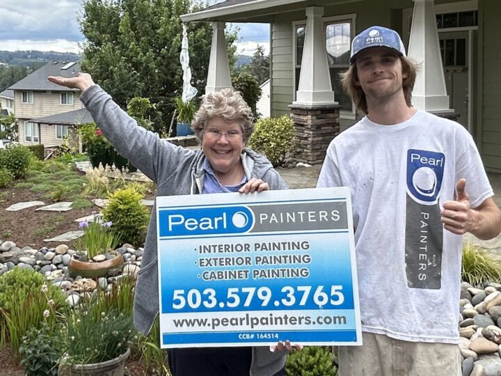 Two people stand in front of a house, holding a sign for "Pearl Painters" offering interior, exterior, and cabinet painting services, with contact information and website URL included.