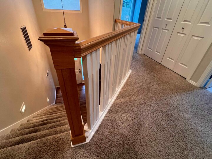 The carpeted stairway, enhanced with a sleek Bull Mountain Handrail, leads gracefully down to a lower floor. It's adjacent to pristine white closet doors and illuminated by a modern wall-mounted light, creating a market-ready aesthetic.