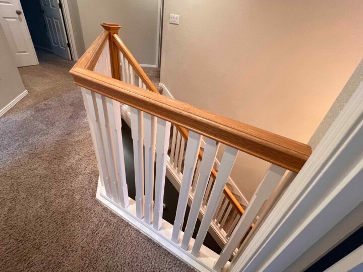 View of a carpeted staircase with a sleek Bull Mountain Handrail and white balusters, leading down to the lower floor, offering a modern touch that's market-ready.