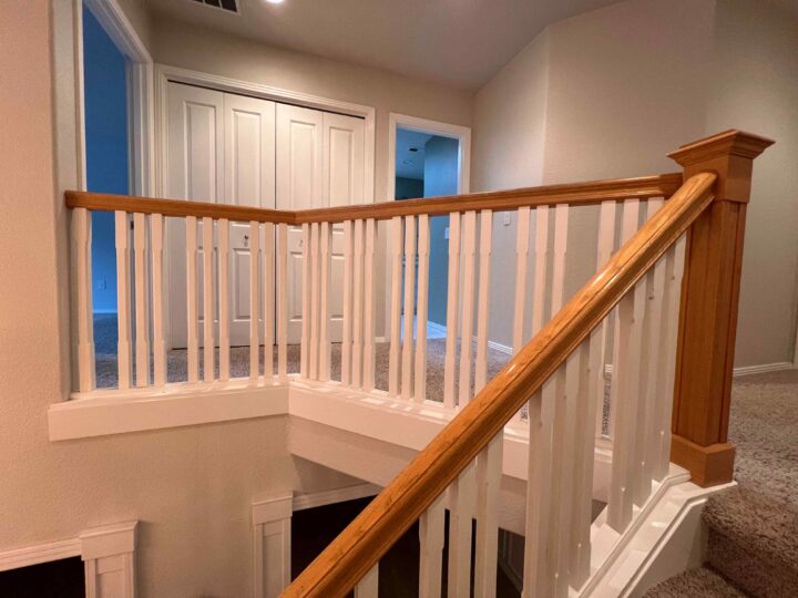 A sleek Bull Mountain handrail with wooden elegance and white spindles guides you to a carpeted hallway and closed white doors, adding a touch of modern sophistication to the home's interior.