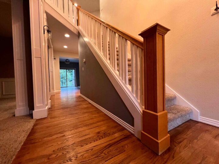 A wooden staircase with carpeted steps and a Bull Mountain Handrail adds a modern look to the house's interior, perfectly complementing the hardwood floor.