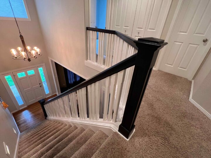 The carpeted staircase, featuring a Bull Mountain Handrail with a modern look, leads to a landing. A chandelier elegantly hangs above, illuminating the space and highlighting the front door with sidelights visible below—truly market-ready elegance at its finest.