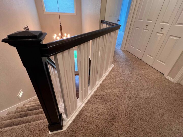 The carpeted staircase, featuring a sleek Bull Mountain Handrail, leads to a hallway with closed white doors and a chandelier visible below.