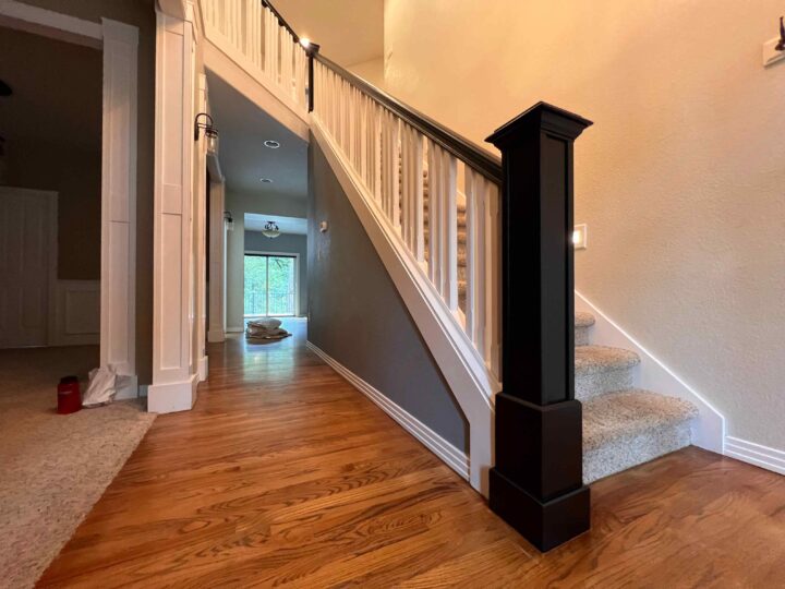 A wooden staircase with beige carpeted steps and a Bull Mountain handrail leads upstairs, offering a modern look. The surroundings include a hardwood floor and a perpendicular hallway with a distant view of a window, making the space market-ready.