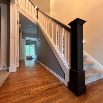 A staircase with wooden steps and a Bull Mountain Handrail is shown, leading to an upper level. The surrounding area, designed for a modern look, features wood and carpet flooring, creating a market-ready appeal.