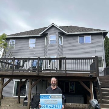 Scott holds a Pearl Painters sign in front of a two-story gray house with a wooden deck in Portland, advertising interior and exterior painting for April 2025.