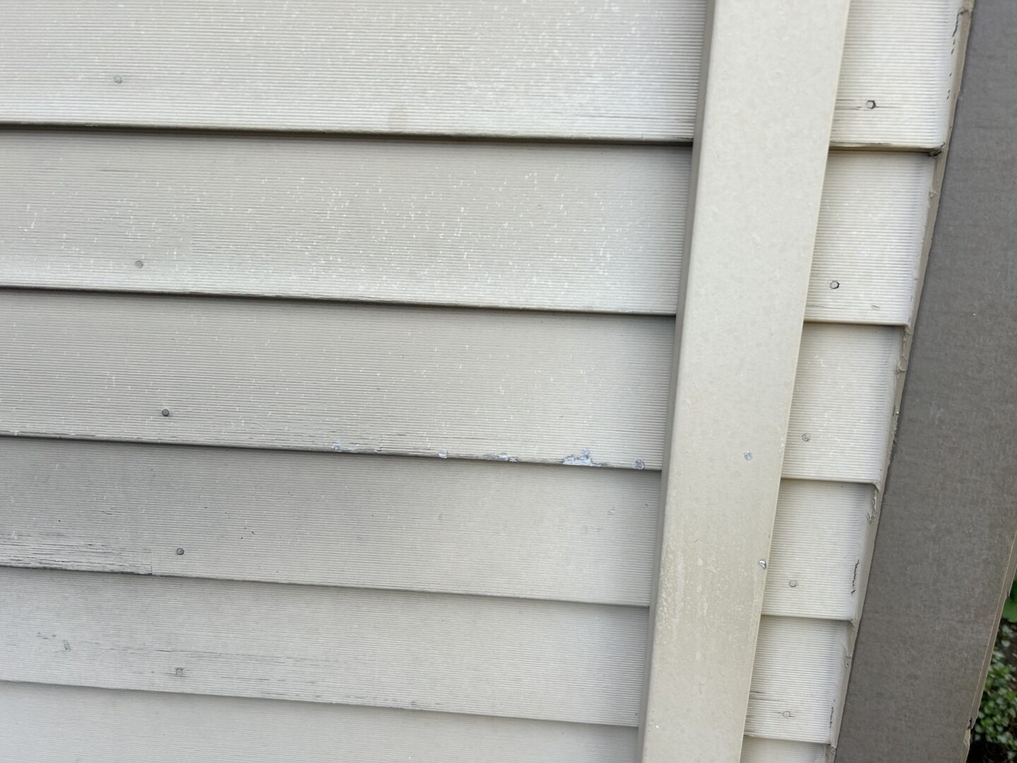 Close-up view of slightly weathered house exterior siding, showing minor chipping and paint issues.