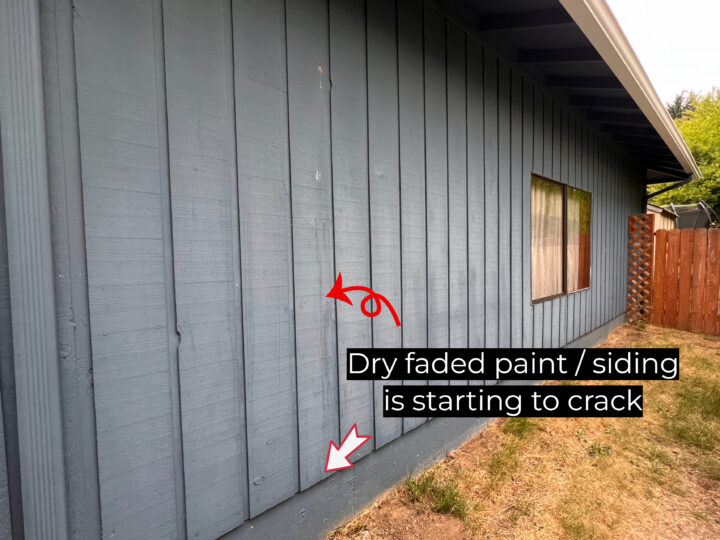 A blue wooden exterior wall of a house with dry, faded paint shows signs of cracking on the siding. There is a window and a red arrow pointing to the cracks with a text overlay indicating exterior painting problems.