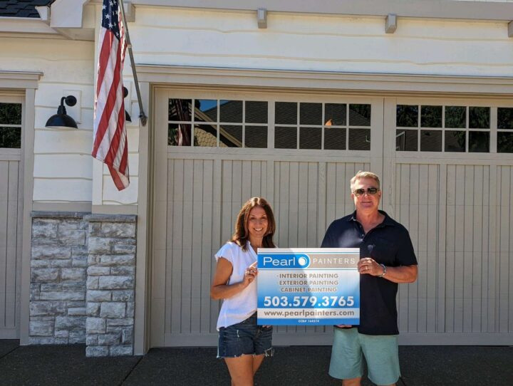 Two people stand in front of a garage in Portland, holding a Pearl Painters sign for painting services; an American flag is visible on the left.
