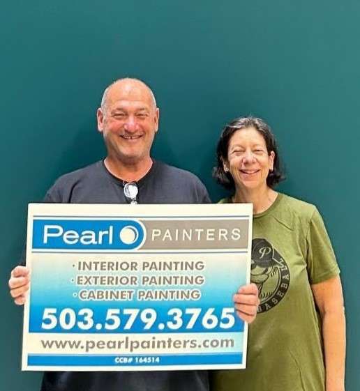 Two people stand in front of a teal wall in Portland, smiling and holding a Pearl Painters sign with painter services and contact details.