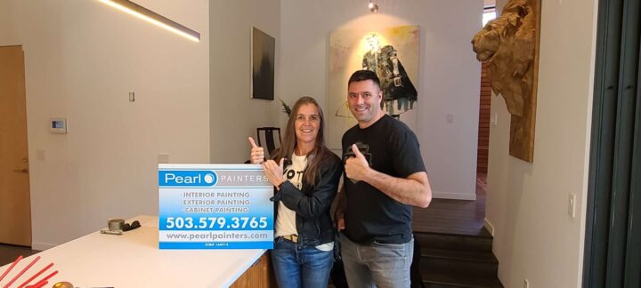 Two people stand in a modern kitchen in Portland holding a Pearl Painters sign with painting services and contact details.