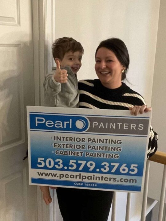 A woman and a young boy hold a Pearl Painters sign advertising interior, exterior, and cabinet painting in Portland; the boy gives a thumbs up.