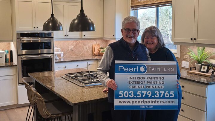 Two people stand in a kitchen in Portland holding a Pearl Painters sign advertising interior, exterior, and cabinet painting.