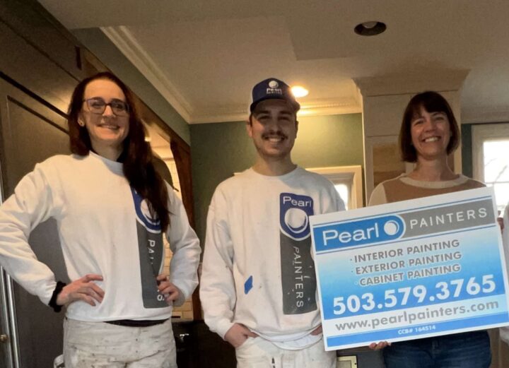 Three people, including two in Pearl Painters uniforms, stand indoors in Portland holding a sign advertising interior, exterior, and cabinet painting services with contact details.