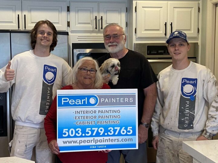 Four people and a small dog pose in a kitchen. Two painters wear Pearl Painters shirts and hold a sign with painting services and contact details. Location: Portland.