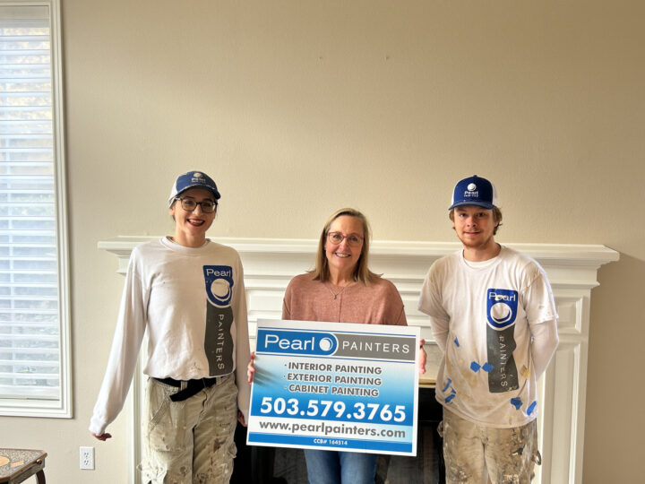 Three people pose indoors in Portland: two painters in paint-splattered work clothes and one in casual clothes, holding a Pearl Painters sign with contact information.