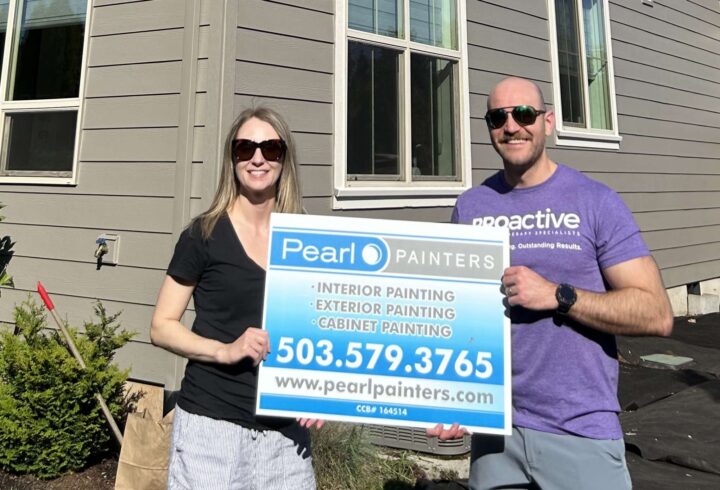 Two people stand outside a house in Portland holding a Pearl Painters sign advertising interior, exterior, and cabinet painting services.