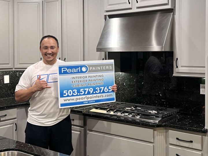 A person in a modern Portland kitchen holds a Pearl Painters sign advertising local painting services, with contact details shown.
