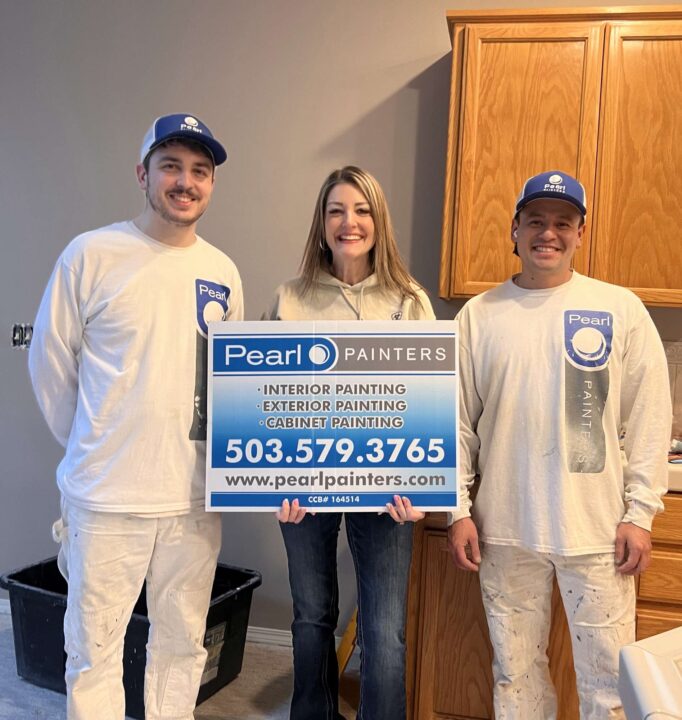 Three painters stand indoors in Portland; two wear white uniforms, and one holds a Pearl Painters sign advertising interior, exterior, and cabinet painting.