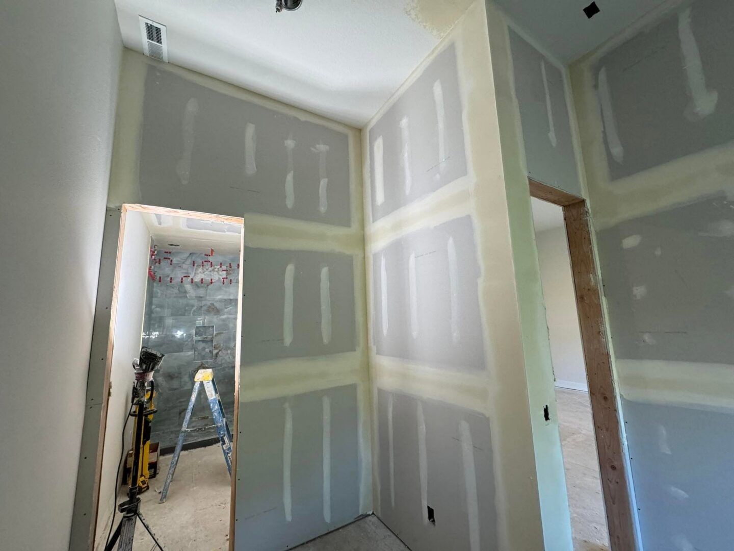 A room in Portland under construction with unfinished drywall, exposed seams, a doorway on the left, and painting tools visible—Pearl Painters at work.