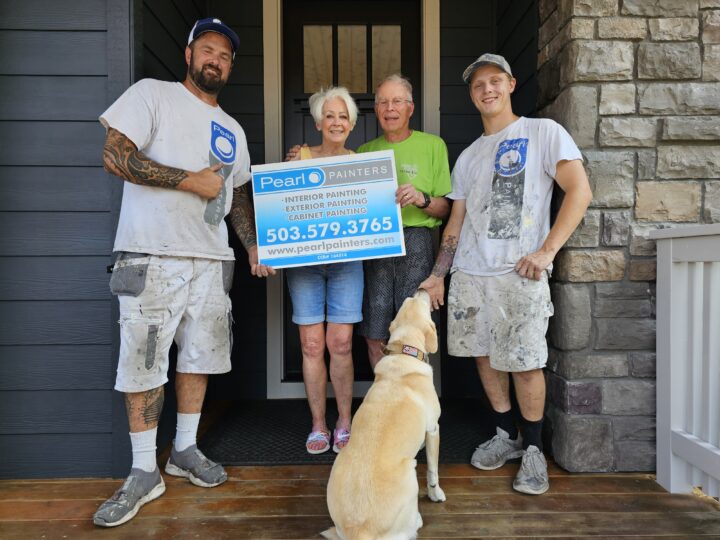 Two painters and a couple with a yellow dog stand on a porch, smiling, holding a Pearl Painters sign in Portland.