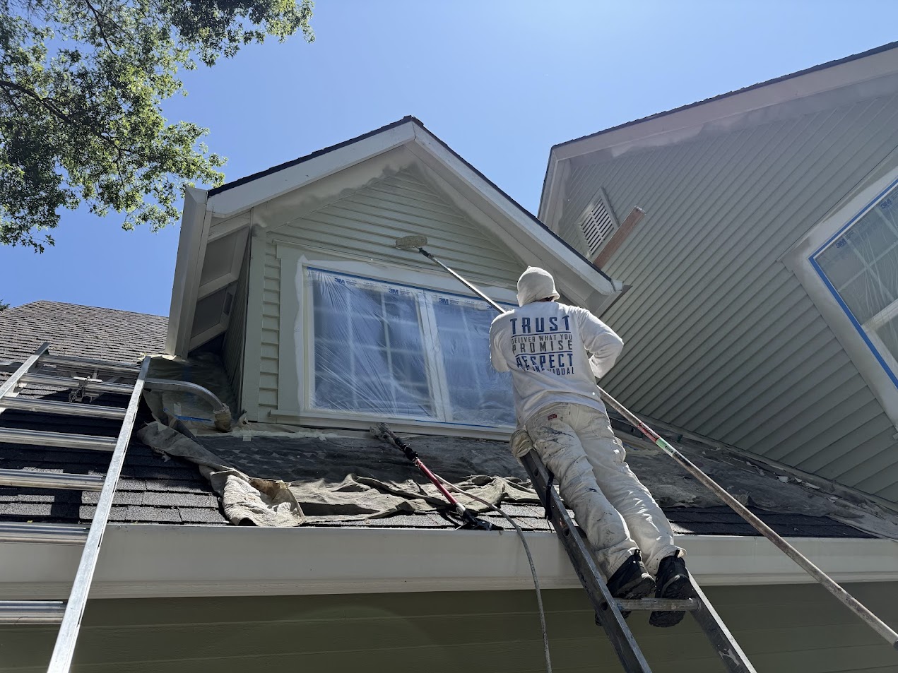 A painter with Pearl Painters paints the exterior of a Kearns house near a second-story window covered in plastic sheeting, June 2025.