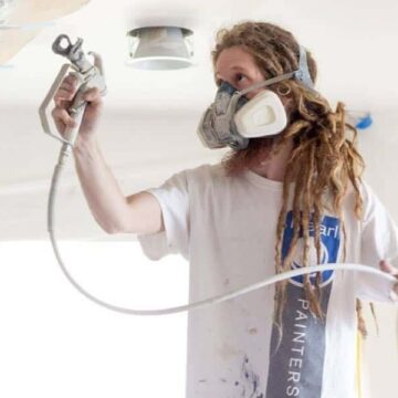 Zak with Pearl Painters wearing a respirator mask and using a paint sprayer.