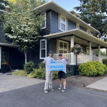 Two men standing in front of a house in the West Linn Neighborhood, with a sign advertising an Exterior Paint Job.