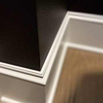 Close-up of a white baseboard against a black wall with a wooden floor.