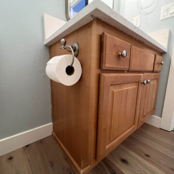 A toilet paper holder in a bathroom with wood floors undergoes a cabinet update in Northwest Portland.