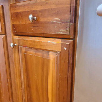 Wooden kitchen cabinets with visible scratches and wear near a stainless steel appliance.