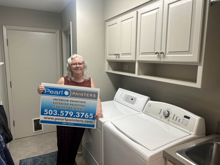 Deanne smiles while holding a Pearl Painters sign in her freshly painted laundry room in Portland.