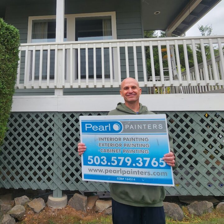 Man in front of house holds Pearl Painters sign for Portland painting services—interior, exterior, and cabinets—with contact info.