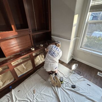 A man meticulously painting a built-in cabinet in a showstopper home office.