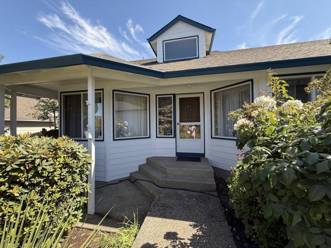 A white house with blue trim in Portland, painted by Pearl Painters, with porch, big windows, glass door, and green shrubs.