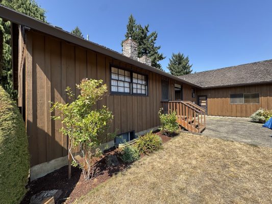 Brown wooden house with porch, stairs, garden shrubs; painted in Craytor by Pearl Painters. Painter style; not Portland.