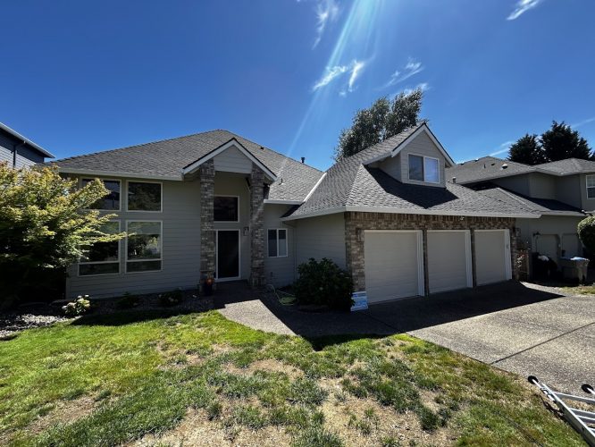 A painter from Pearl Painters paints a beige, two-story Featherstone house with stone accents and double garage in Portland.
