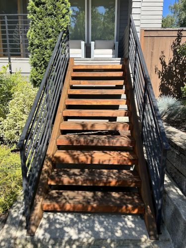 A wooden staircase with black railings leads to a glass door, greenery around. Painted by Pearl Painters, Portland, July 2025.