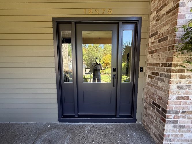 Gray door, glass panels, beige wall, 18375 above; brick right. Painter's reflection visible. Painted by Pearl Painters in Buck.