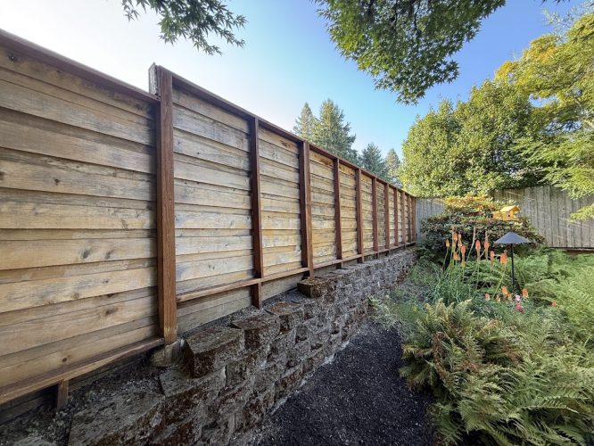 Wooden fence with vertical supports on a stone wall and garden, Harvey, July 2025. Pearl Painters painting project.